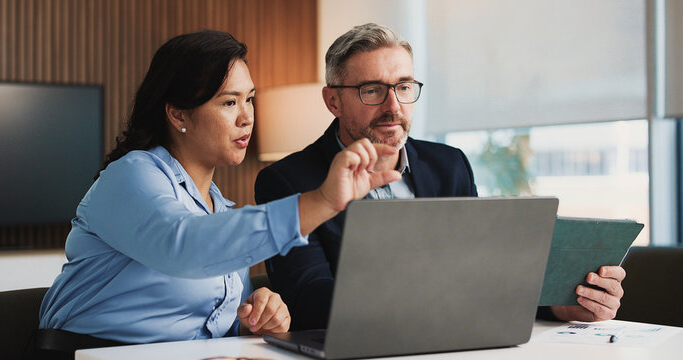 Two business professionals reviewing a laptop and tablet during a budget planning meeting.