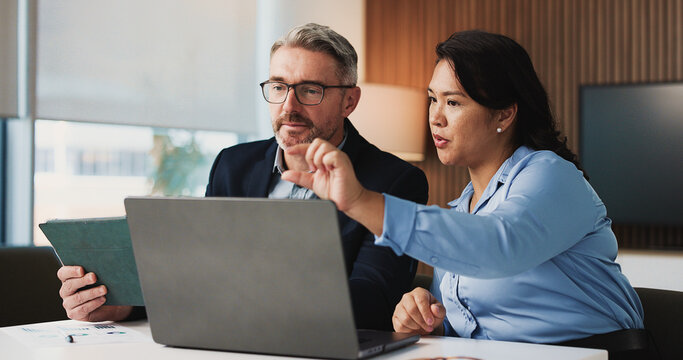 Two business professionals reviewing a laptop and tablet during an IT budget planning meeting.